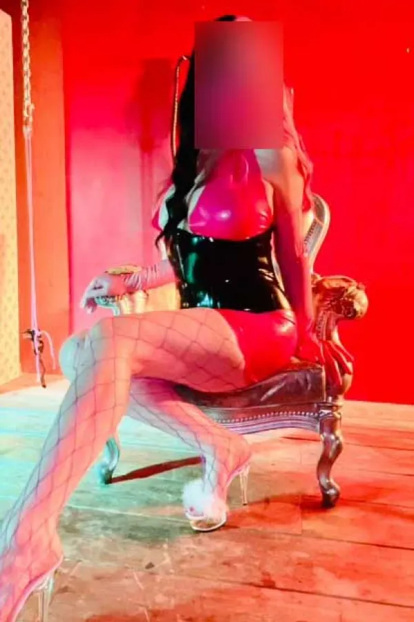 Erin sitting on a silver throne while wearing a pink latex dress 